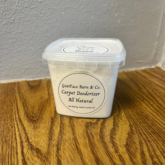Container of Goatfac Barn & Co. Carpet Deodorizer on a wooden floor with a gray wall background
